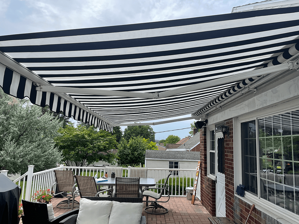 black and white canvas retractable awning installed on a brick home over the patio